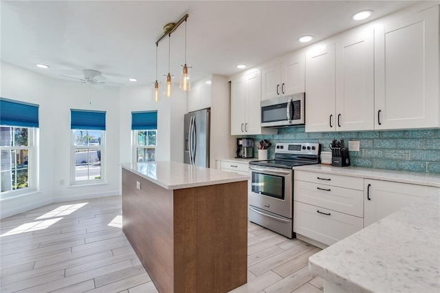 kitchen with light wood-type flooring, stainless steel appliances, a kitchen island, pendant lighting, and white cabinetry