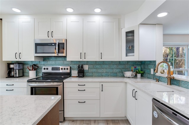 kitchen featuring decorative backsplash, appliances with stainless steel finishes, light wood-type flooring, sink, and white cabinets