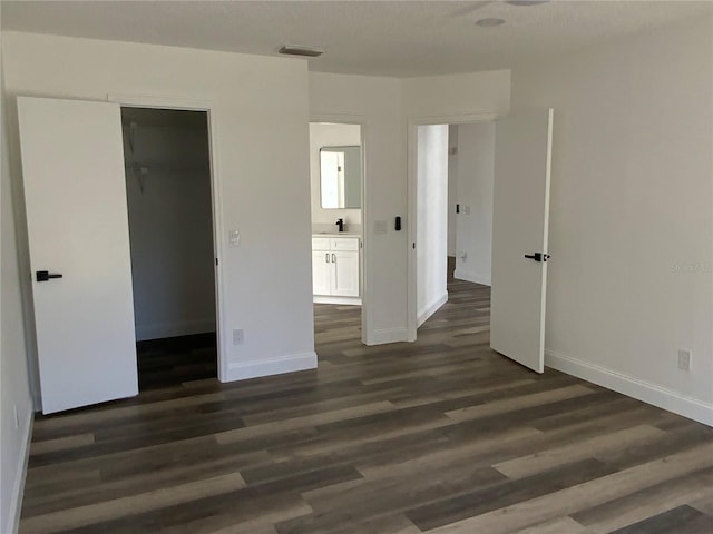 unfurnished bedroom with ensuite bathroom, dark hardwood / wood-style flooring, a spacious closet, and a closet