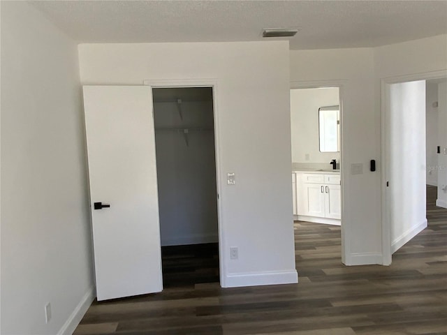 unfurnished bedroom featuring a walk in closet, dark wood-type flooring, and ensuite bath