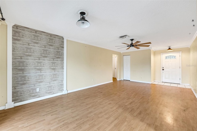 unfurnished living room featuring wood walls, crown molding, ceiling fan, a textured ceiling, and light hardwood / wood-style floors