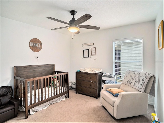 bedroom featuring a textured ceiling, ceiling fan, a crib, and light carpet