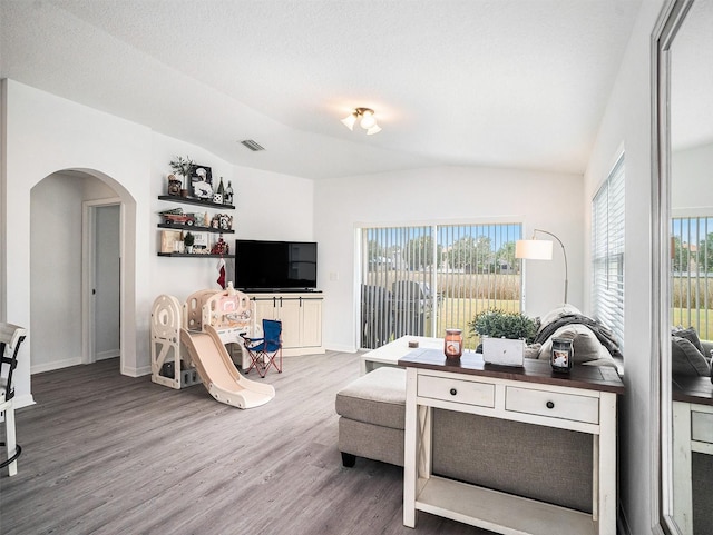 living area with arched walkways, wood finished floors, visible vents, and plenty of natural light