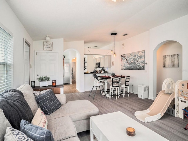 living room featuring arched walkways, visible vents, and wood finished floors