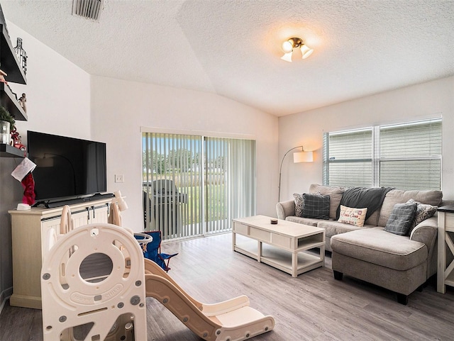 living area featuring visible vents, light wood-type flooring, lofted ceiling, and a healthy amount of sunlight