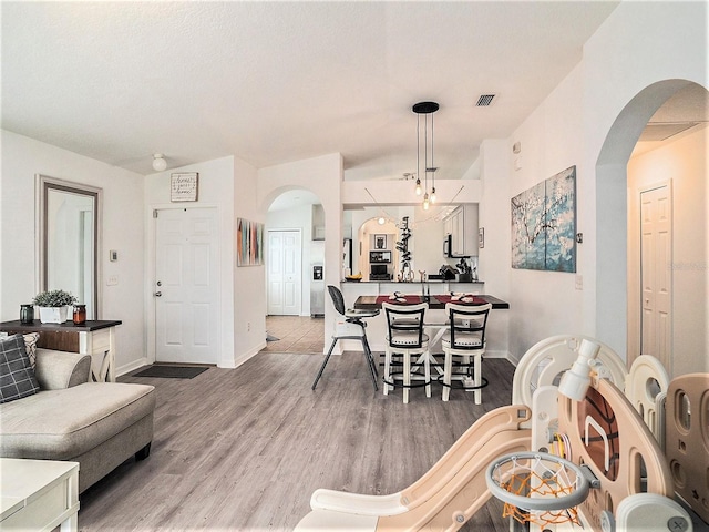 living room featuring baseboards, arched walkways, wood finished floors, and lofted ceiling