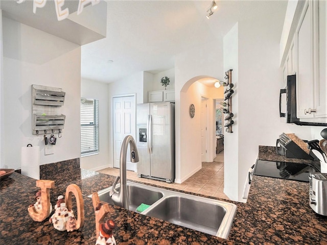 kitchen featuring stainless steel fridge, black microwave, white cabinetry, arched walkways, and a sink