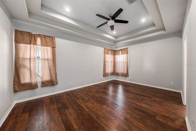 spare room with a raised ceiling, ceiling fan, and dark hardwood / wood-style flooring