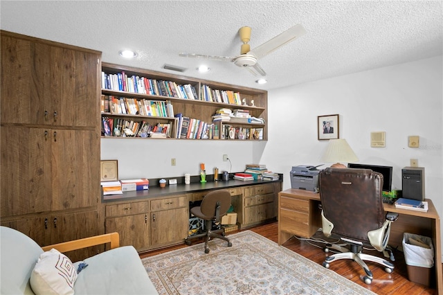 office with built in desk, a textured ceiling, ceiling fan, and dark wood-type flooring