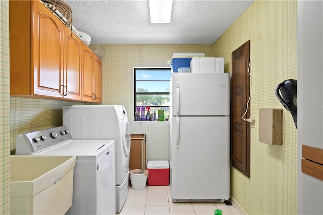 clothes washing area featuring cabinets, independent washer and dryer, a textured ceiling, and light tile patterned floors