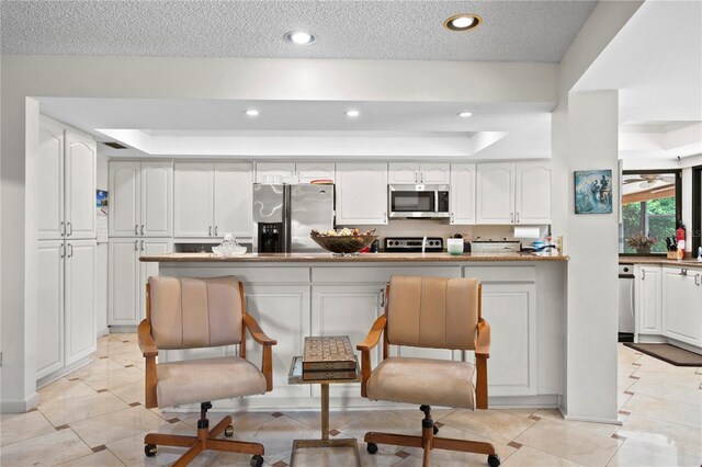 kitchen featuring a raised ceiling, a textured ceiling, appliances with stainless steel finishes, white cabinetry, and a breakfast bar area