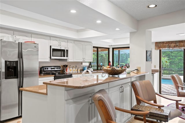 kitchen with a wealth of natural light, light stone countertops, white cabinetry, and appliances with stainless steel finishes