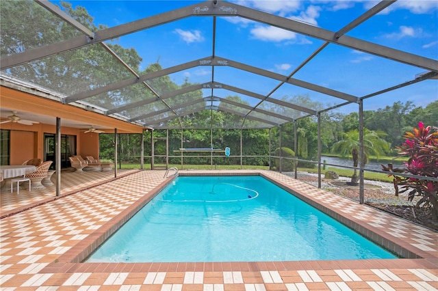 view of pool with glass enclosure, ceiling fan, a patio area, and a water view