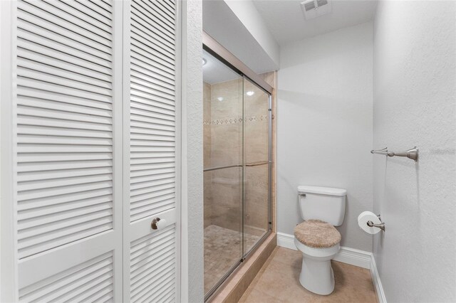 bathroom featuring tile patterned floors, a shower with door, and toilet