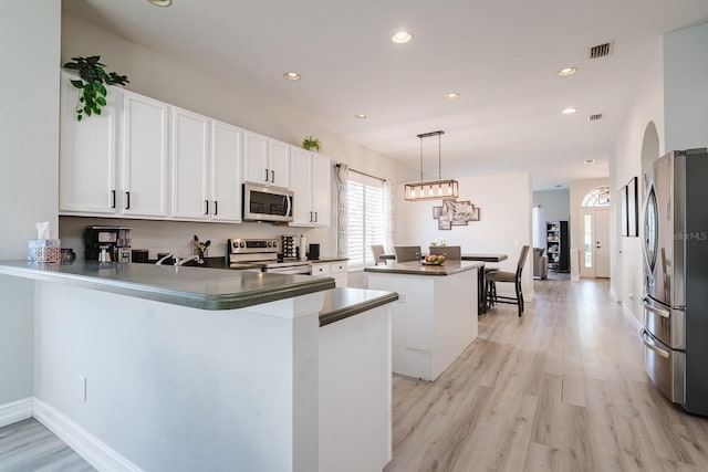 kitchen featuring white cabinets, kitchen peninsula, stainless steel appliances, and hanging light fixtures