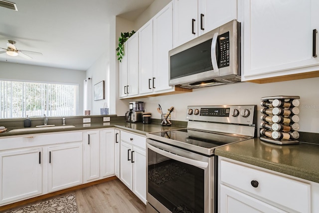 kitchen with appliances with stainless steel finishes, light wood-type flooring, ceiling fan, sink, and white cabinetry