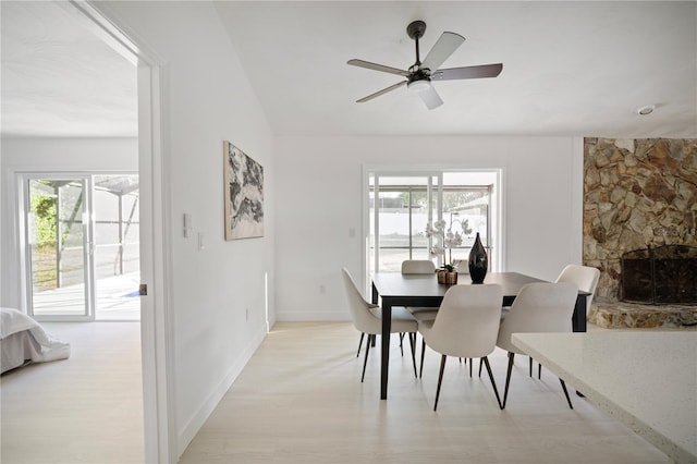 dining room with a stone fireplace, a wealth of natural light, ceiling fan, and light hardwood / wood-style floors