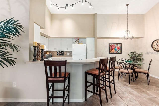 kitchen with kitchen peninsula, white fridge, pendant lighting, a breakfast bar area, and white cabinets