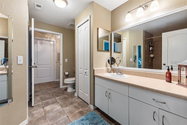 bathroom with a tile shower, tile patterned floors, vanity, and toilet