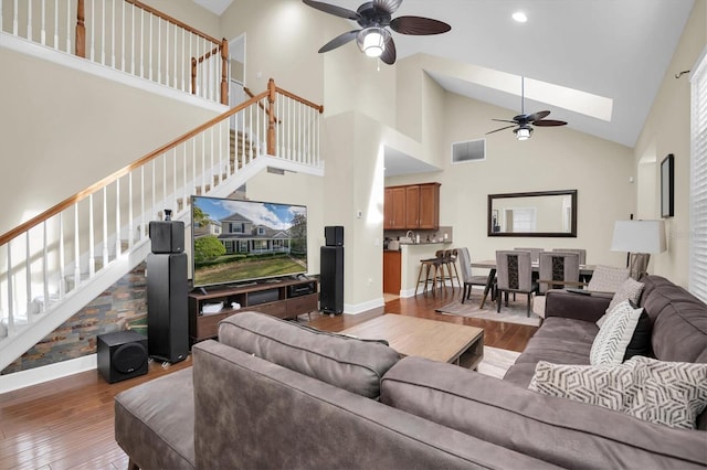 living room featuring ceiling fan, dark wood-type flooring, high vaulted ceiling, and a skylight