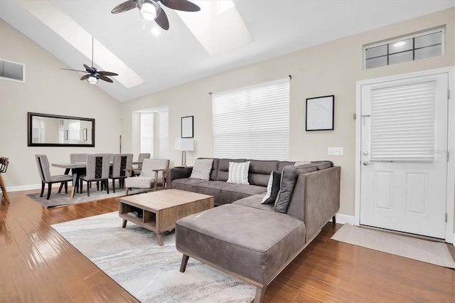 living room with ceiling fan, vaulted ceiling with skylight, and wood-type flooring