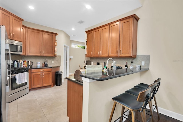 kitchen with decorative backsplash, dark stone countertops, kitchen peninsula, and appliances with stainless steel finishes