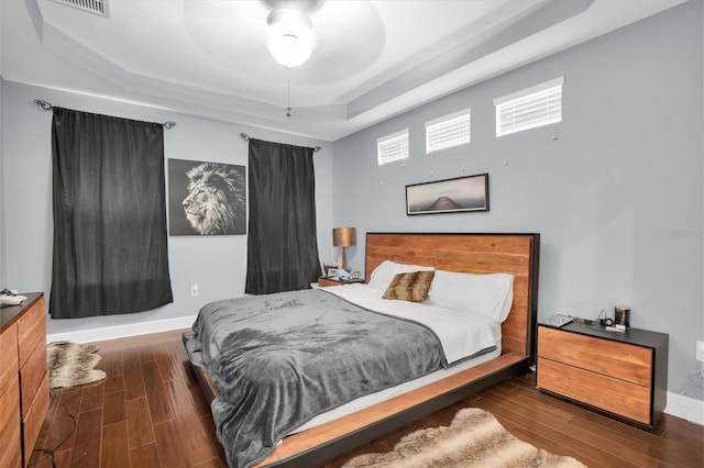 bedroom with dark hardwood / wood-style flooring, a tray ceiling, and ceiling fan