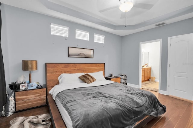 bedroom featuring hardwood / wood-style flooring, ceiling fan, a raised ceiling, and ensuite bath