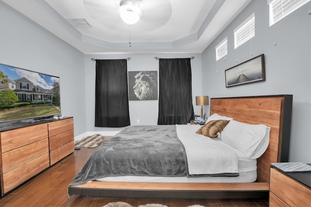 bedroom with a raised ceiling, ceiling fan, and dark hardwood / wood-style floors