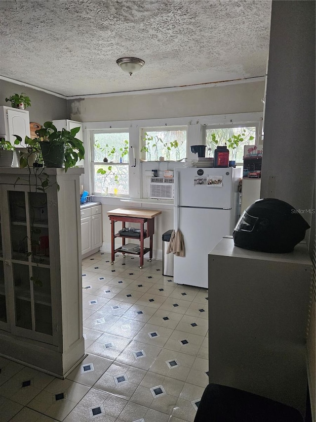 kitchen with white cabinets, white refrigerator, ornamental molding, and a textured ceiling