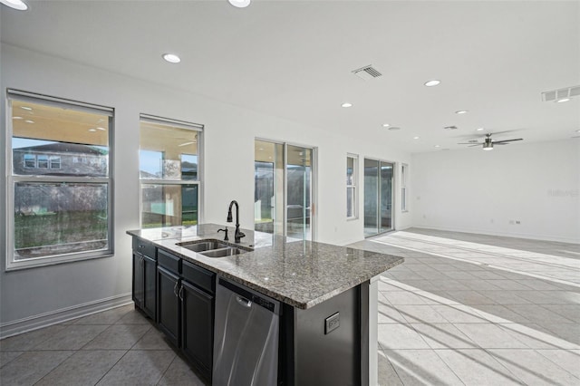 kitchen featuring dishwasher, sink, tile patterned flooring, light stone countertops, and an island with sink