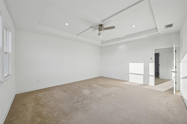 empty room featuring a tray ceiling, light carpet, and ceiling fan