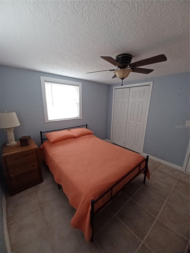 bedroom featuring ceiling fan, a closet, dark tile patterned floors, and a textured ceiling