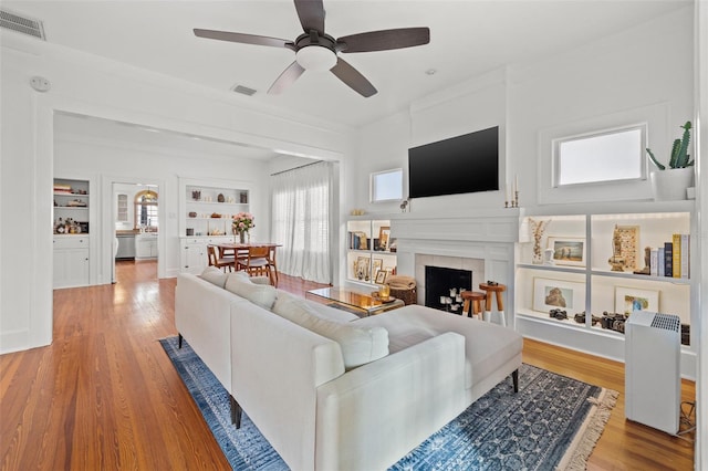 living room featuring a fireplace, built in shelves, ceiling fan, and wood-type flooring