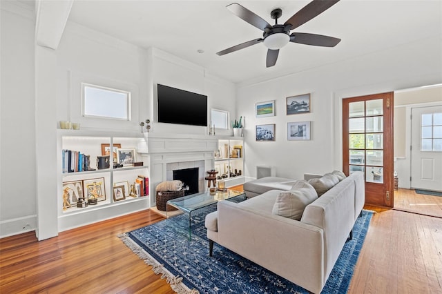 living room with wood-type flooring, ceiling fan, crown molding, and a tiled fireplace