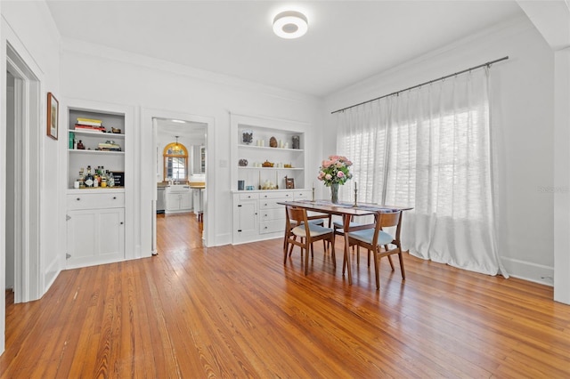 dining room featuring built in shelves, light wood-type flooring, plenty of natural light, and crown molding