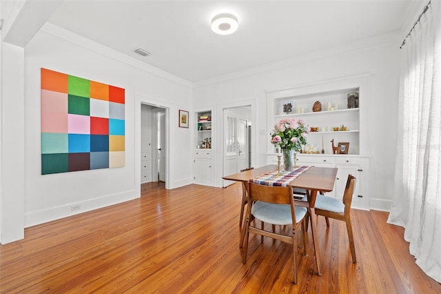 dining space featuring built in shelves, hardwood / wood-style flooring, and crown molding