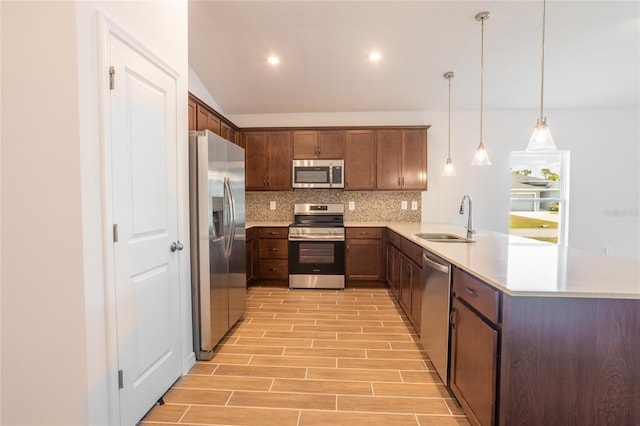 kitchen featuring backsplash, hanging light fixtures, sink, appliances with stainless steel finishes, and kitchen peninsula