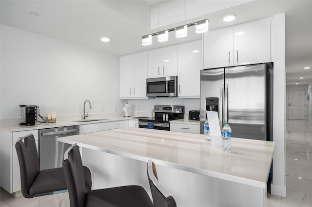 kitchen with a kitchen bar, appliances with stainless steel finishes, hanging light fixtures, sink, and white cabinets