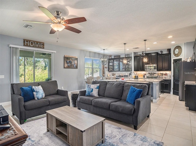 tiled living room with sink, ceiling fan with notable chandelier, and a textured ceiling