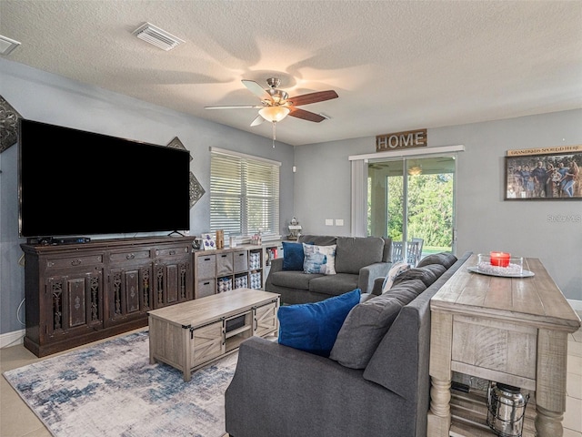 living room with ceiling fan, light tile patterned flooring, and a textured ceiling