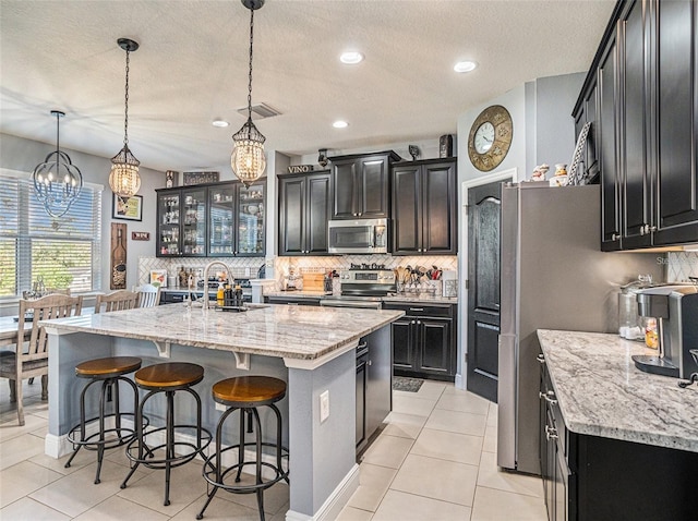 kitchen with sink, hanging light fixtures, stainless steel appliances, an island with sink, and a textured ceiling