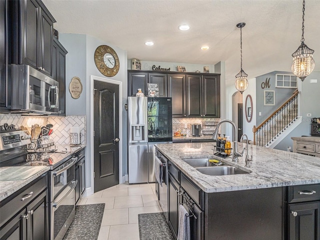 kitchen with sink, stainless steel appliances, an island with sink, decorative light fixtures, and light tile patterned floors