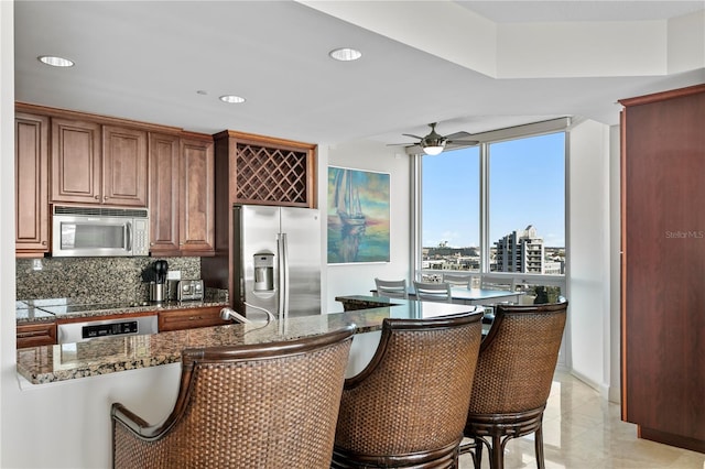 kitchen featuring ceiling fan, stainless steel appliances, backsplash, dark stone counters, and light tile patterned flooring