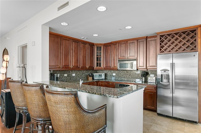 kitchen with backsplash, dark stone countertops, kitchen peninsula, and stainless steel appliances