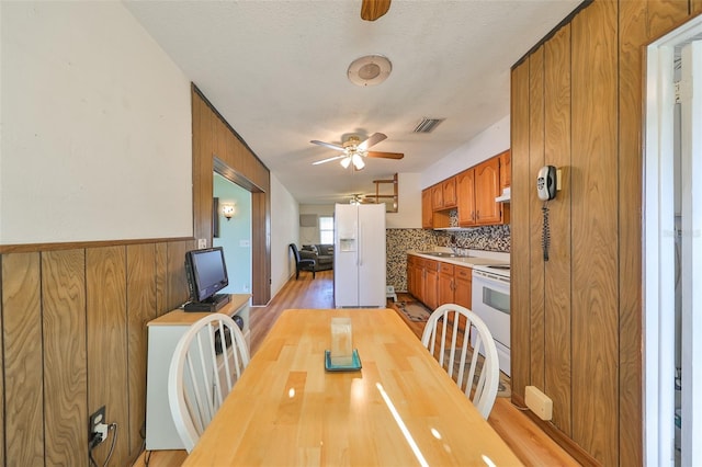 dining space featuring wooden walls, light hardwood / wood-style flooring, ceiling fan, and a textured ceiling