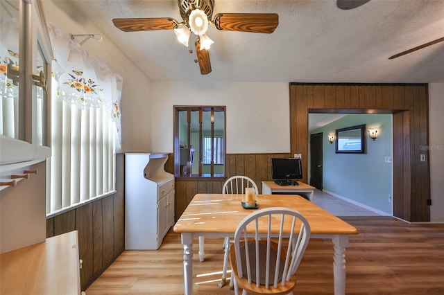 dining room featuring a wealth of natural light, light hardwood / wood-style floors, a textured ceiling, and wooden walls