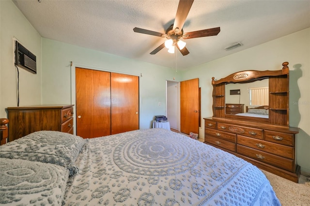 carpeted bedroom featuring a wall mounted air conditioner, ceiling fan, a textured ceiling, and a closet