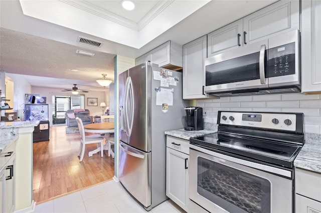 kitchen with light stone countertops, stainless steel appliances, backsplash, light hardwood / wood-style floors, and ornamental molding