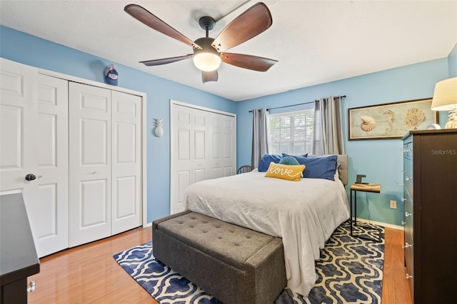 bedroom with hardwood / wood-style floors, ceiling fan, and two closets